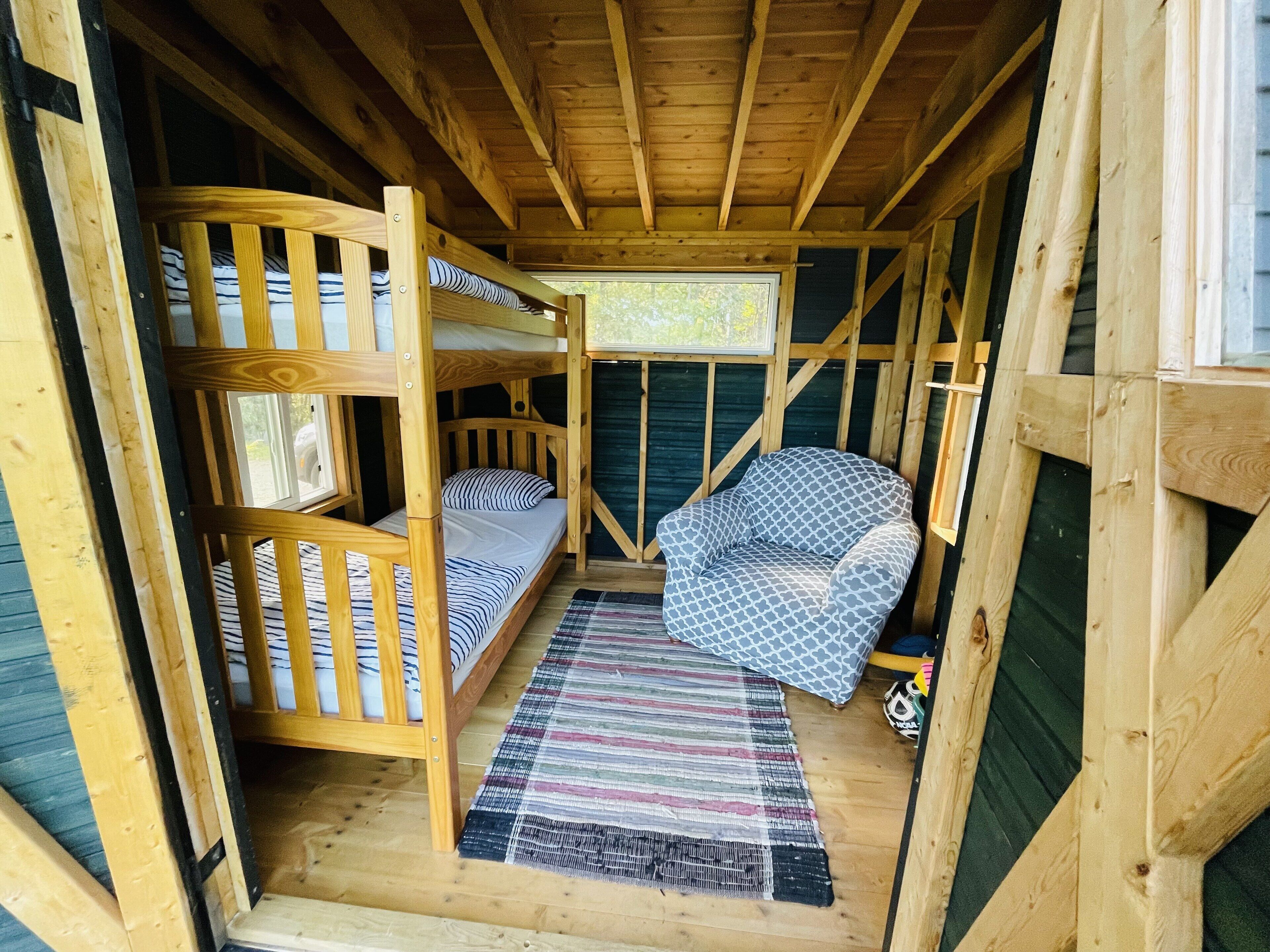 Interior acogedor de una cabaña con literas, una cama individual, un sillón estampado y una alfombra colorida.