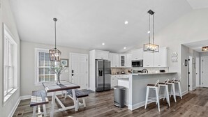 Une cuisine moderne avec des meubles blancs, un réfrigérateur en acier inoxydable et un coin bar équipé de tabourets.