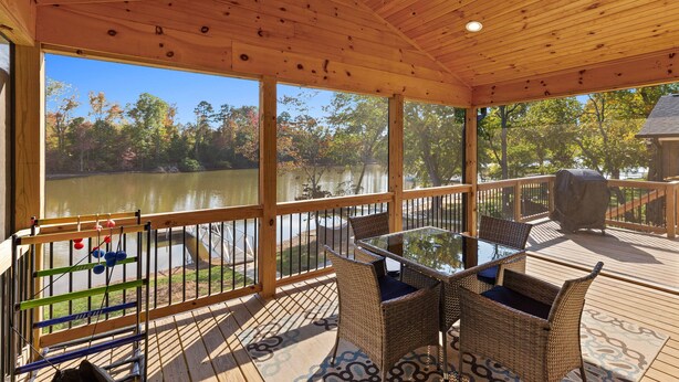 Une terrasse en bois avec une table en verre et des chaises en osier, donnant sur un lac.