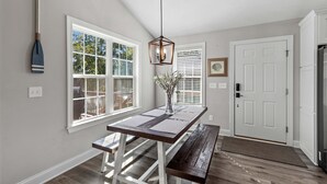 Une cuisine avec une table en bois, un banc, un luminaire suspendu et une porte avec un paillasson.