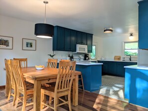 A modern kitchen with wooden dining table and chairs, blue cabinets, and a central island.