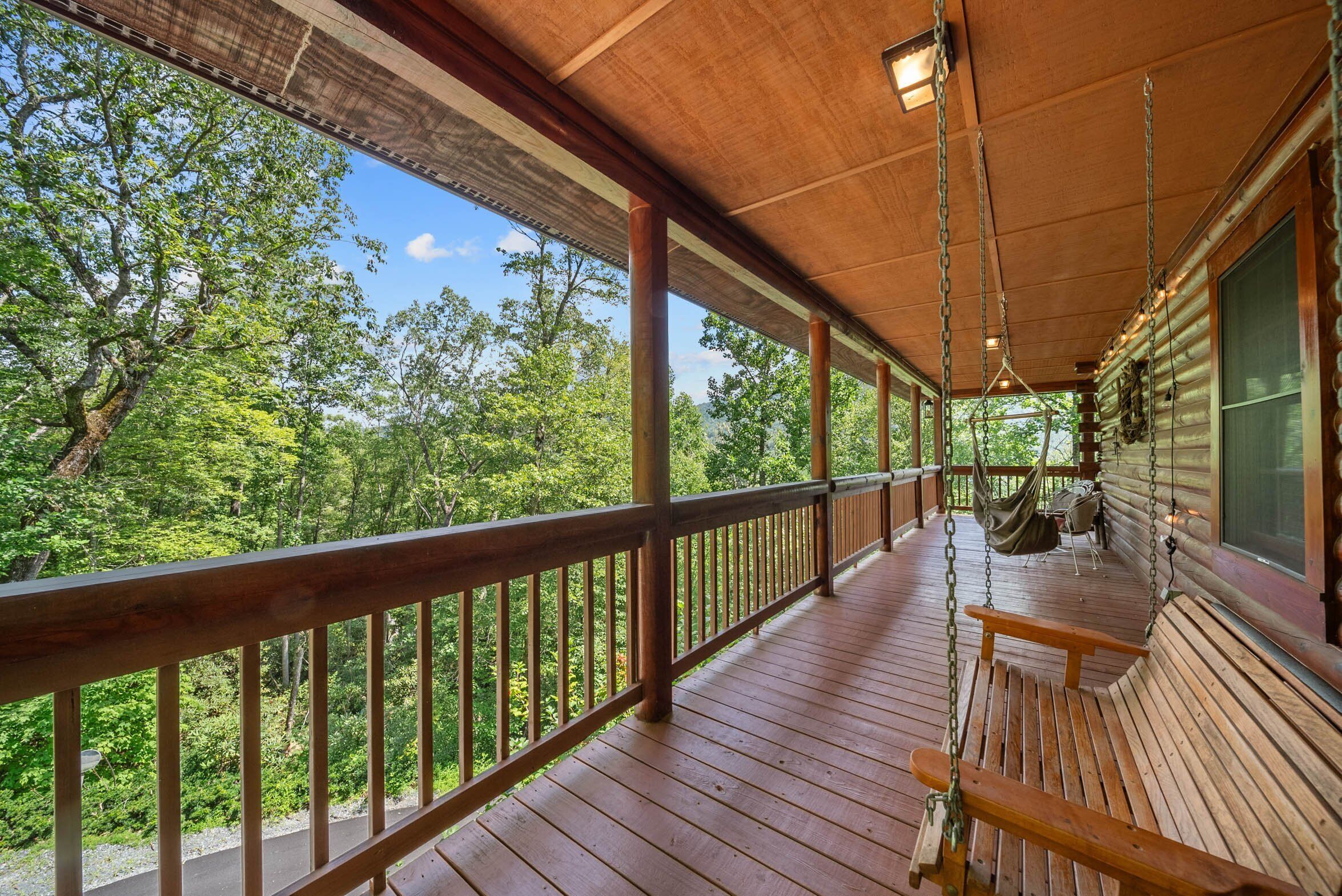 A wooden deck with a swing chair and hanging lights, overlooking a forested area.