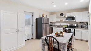 Uma cozinha compacta com armários brancos, geladeira, micro-ondas e um espaço de refeições com mesa posta para dois.