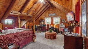 Quarto de cabana de tronco com uma cama, uma escrivaninha, uma cadeira, uma mesa redonda e um ventilador de teto.