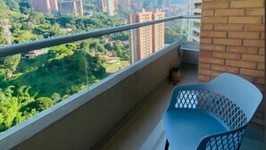 A balcony with a view of a cityscape, a brick wall, and two blue chairs.