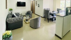 A modern living room with a grey sofa, a round ottoman, and a dining area with a table and chairs.