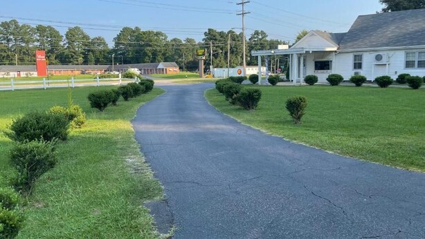 A road leading to a white building with a porch, surrounded by well-maintained grass and small bushes. - Kenwood Court Motel (Wilson)