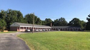 A motel with a long row of rooms, a parking lot, and a grassy area. - Kenwood Court Motel (Wilson)