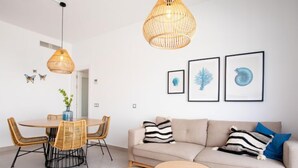 Ein modernes Wohnzimmer mit einem beigen Sofa, zwei runden Tischen, einem Esstisch mit Korbstühlen und einer Pendelleuchte.