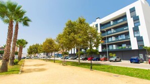Ein modernes Gebäude mit mehreren Etagen und Balkonen, umgeben von einem Parkplatz und Palmen.