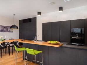 A modern kitchen with a central island, black bar stools, and a dining area with chairs. - Old Olive I by Interhome (Pula/Vodnjan)