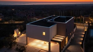 Una casa moderna con tetto piatto, un piccolo portico e vista sul tramonto.