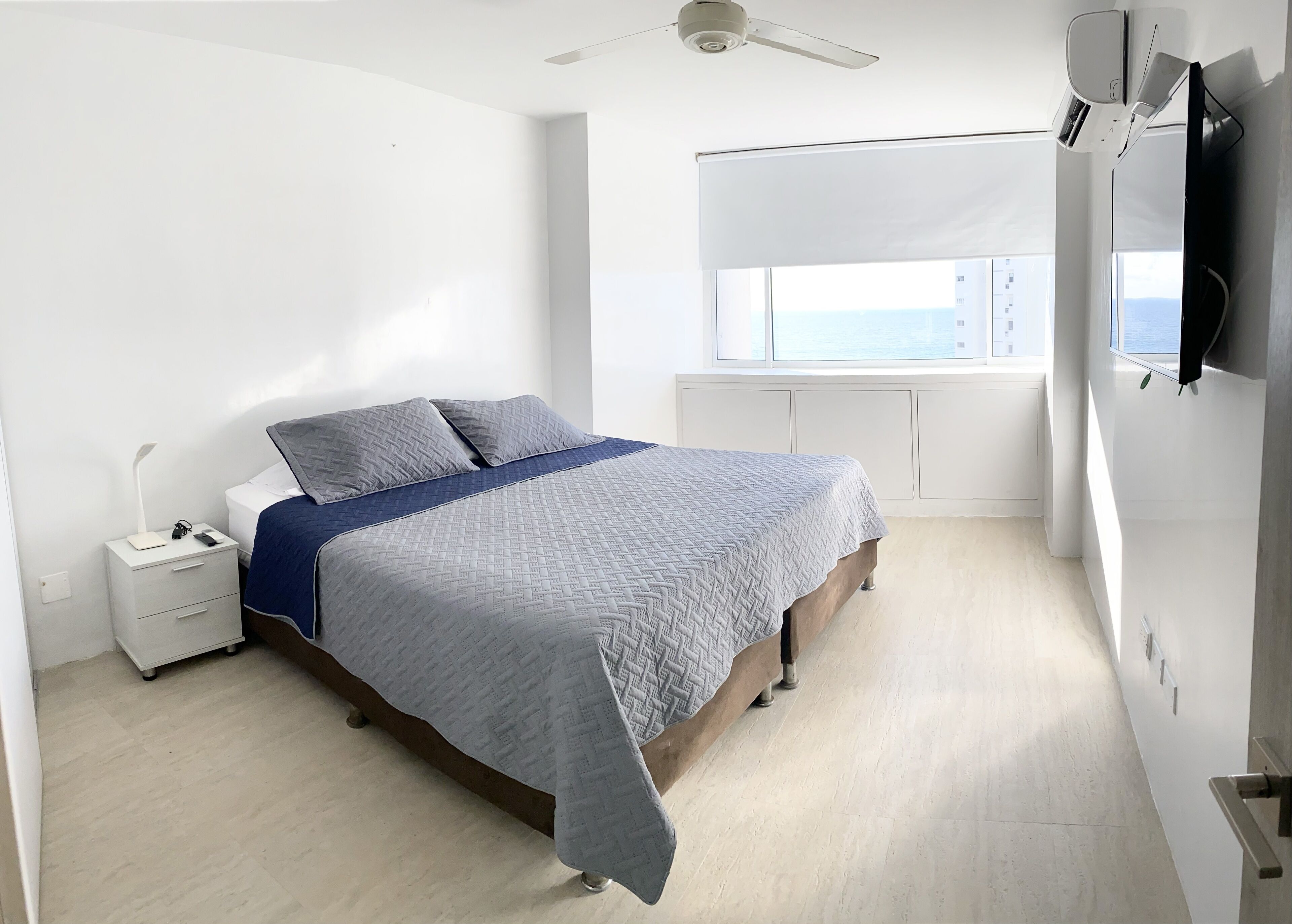 Un dormitorio moderno con cama, mesita de noche y un ventanal con vistas.