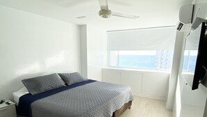 A bedroom with a bed, a nightstand, a window with a view of the sea, and a ceiling fan. - 3TC10 Apartamento Cartagena frente al mar (Cartagena)