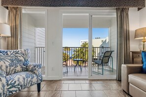 A hotel room with a sliding glass door leading to a balcony, a sofa, a chair, and a table.