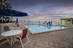 A pool area with lounge chairs and umbrellas, a view of the ocean, and a lifeguard stand.