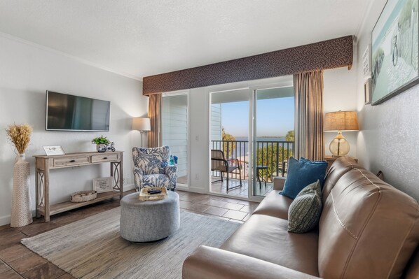 A modern living room with a sofa, ottoman, and a flat-screen TV. - Waterfront condo with sunset views of Tampa Bay. (Tampa)