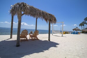 A beach with wooden chairs, a swing, and thatched umbrellas.