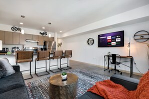 Een moderne woonkamer met een keukenhoek, een flatscreen-televisie aan de wand en een zithoek met een salontafel.