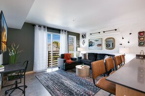 A modern living room with a sofa, chairs, a dining table, and a large window with curtains. - Beacon Hill 1BR - Parking + Workspace - Link Rail - Monthly Stays (Seattle)