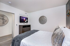 Een moderne slaapkamer met een bed, een flatscreen televisie aan de muur, een ronde decoratieve klok en een grote wereldkaart.