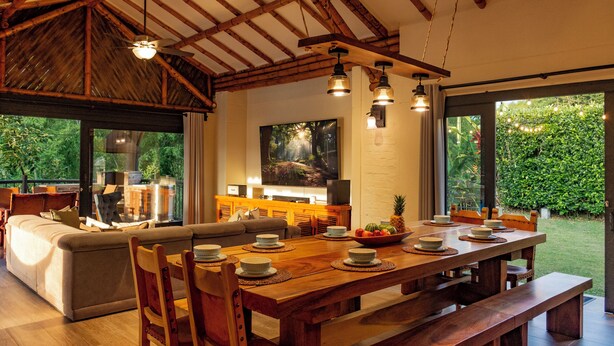 A spacious living area with a wooden dining table set for a meal, a comfortable sofa, and a television in the background. - Luxury Villa • Pool • Jacuzzi • Spa • Maid/Cook • 5 min from Panaca Park. (Quindío)