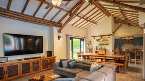 A spacious living room with a large flat-screen TV, a sectional sofa, and a wooden dining table. - Luxury Villa • Pool • Jacuzzi • Spa • Maid/Cook • 5 min from Panaca Park. (Quindío)