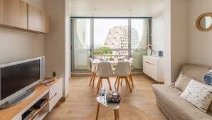 Een moderne woonkamer met een flatscreen televisie, een bank, een eethoek met stoelen en een stadsgezicht door grote ramen.
