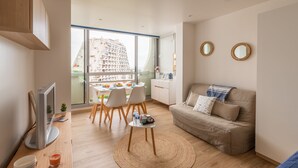 Een moderne woonkamer met een bank, televisie, eethoek en grote ramen met uitzicht op een stadsbeeld.