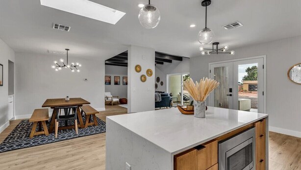 Una cocina moderna con una isla central, iluminación colgante y un comedor con mesa y bancos de madera.