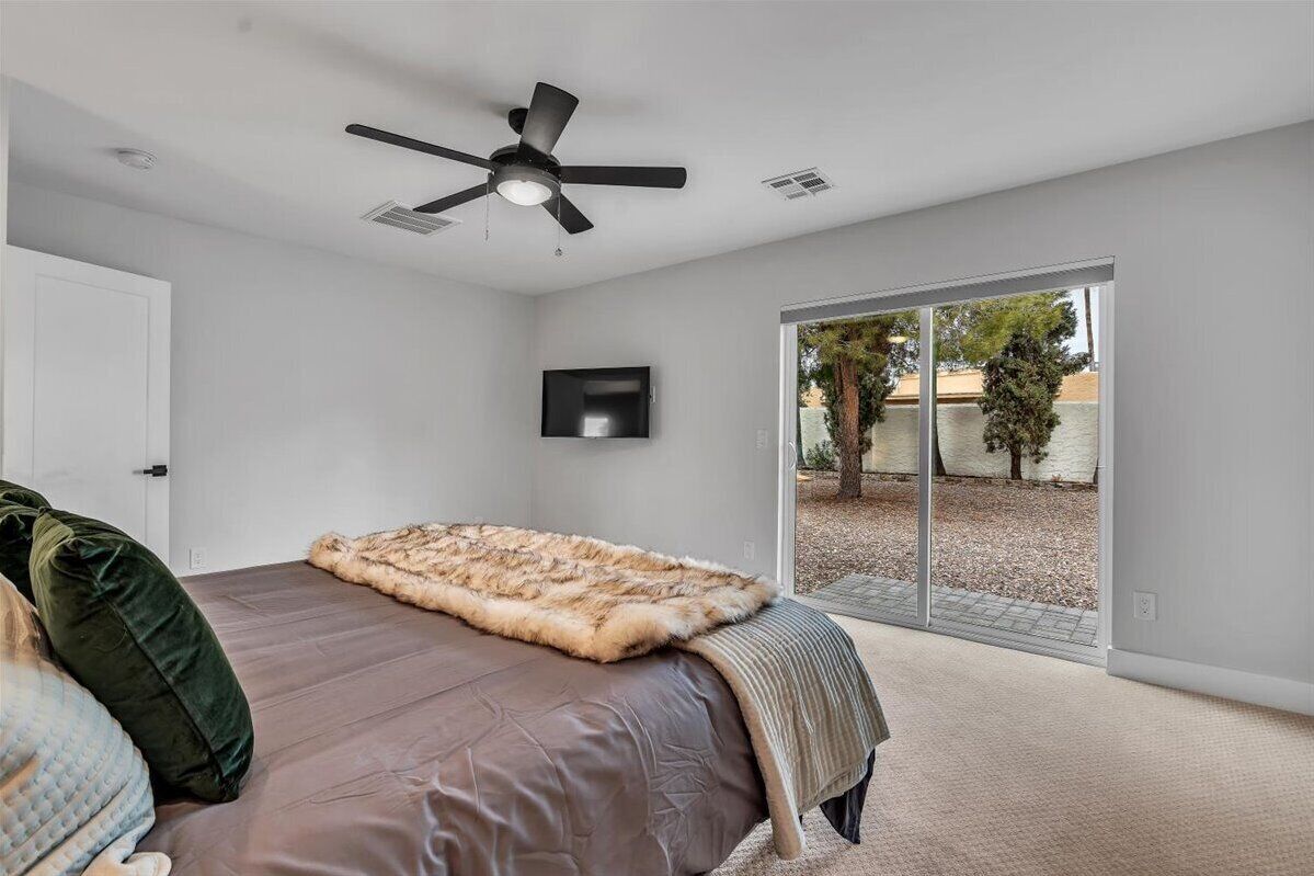 A bedroom with a bed, a ceiling fan, a TV, and a sliding glass door to an outdoor area.