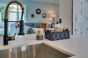 A modern kitchen with a stainless steel sink, a black faucet with a flexible hose, and a storage basket containing kitchen essentials.
