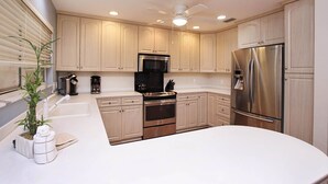 A modern kitchen with light wood cabinets, stainless steel appliances, and a central island. - Sandcastle Home on Sanibel Island in The Dunes Golf Club (Sanibel)
