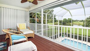 A covered outdoor area with a ceiling fan, wicker furniture, and a view of a swimming pool and greenery. - Sandcastle Home on Sanibel Island in The Dunes Golf Club (Sanibel)