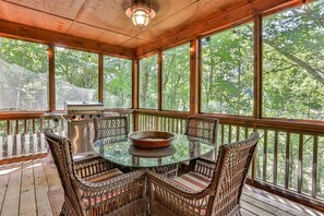 Un espace extérieur abrité, doté d’une table en verre, de chaises en osier et d’un barbecue.