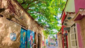 A narrow street lined with colorful buildings, some with murals, and a sign indicating a hotel. - 3G1-1 Apartamento Ciudad Antigua Getsemani (Cartagena)