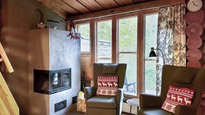 A cozy living room with a fireplace, two armchairs with festive cushions, and large windows offering a view of the outdoors. - Salmikankaan kelo d2 by Interhome (Kuusamo)