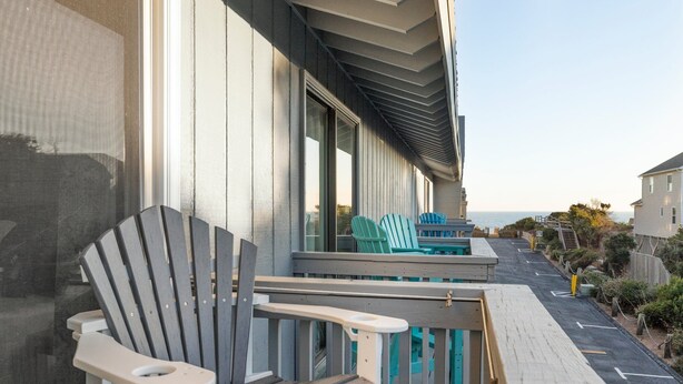 Eine Holzterrasse mit einer Reihe Adirondack-Stühlen und einem kleinen Tisch.