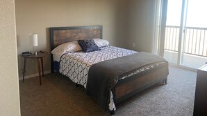 Un dormitorio con cama, una mesita de noche con lámpara, un ventilador de techo y un ventanal grande.