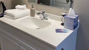 Un baño con lavamanos blanco, un espejo, toallero, una botella y una caja de pañuelos.