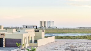 Un bâtiment moderne doté d’un toit plat et d’un garage, offrant une vue sur une plage et des immeubles de grande hauteur situés au loin.