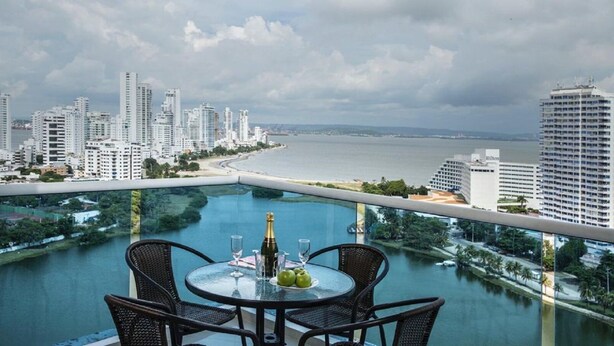 A balcony with a table set for two, overlooking a cityscape and a body of water. - PH17P Penthouse Cartagena Frente al mar (Cartagena)