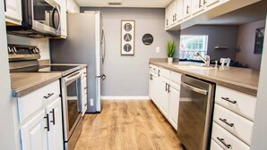 A modern kitchen with white cabinetry, stainless steel appliances, and a wooden floor.