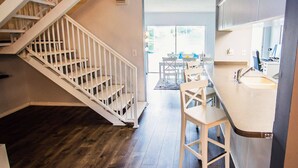 A modern kitchen with white cabinetry, a stainless steel sink, and a wooden staircase.