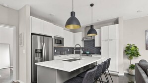 Een moderne keuken met een centraal eiland, roestvrijstalen apparatuur en een zwarte hanglamp.
