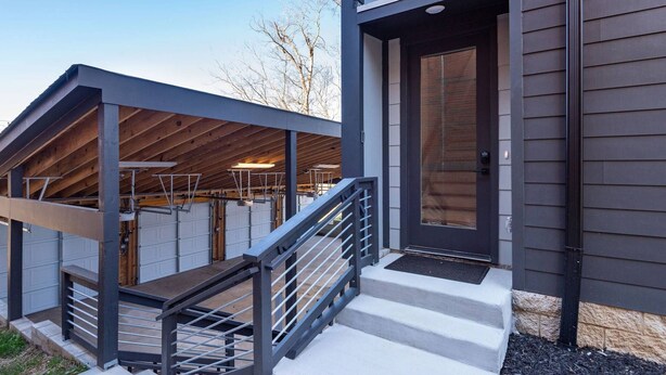 Een modern huis met een overdekte veranda, een trap die naar de ingang leidt, en een garagepoort.