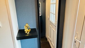 A hallway with a dark blue wall, a black-framed mirror, a small shelf with a golden statue, a wicker basket, and a white door with a window. - Studio near University and Hospital BETHUNE (Beuvry)