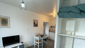 A compact living space with a bed, a TV on a white console, a dining area with a table and chairs, and a kitchenette. - Studio near University and Hospital BETHUNE (Beuvry)