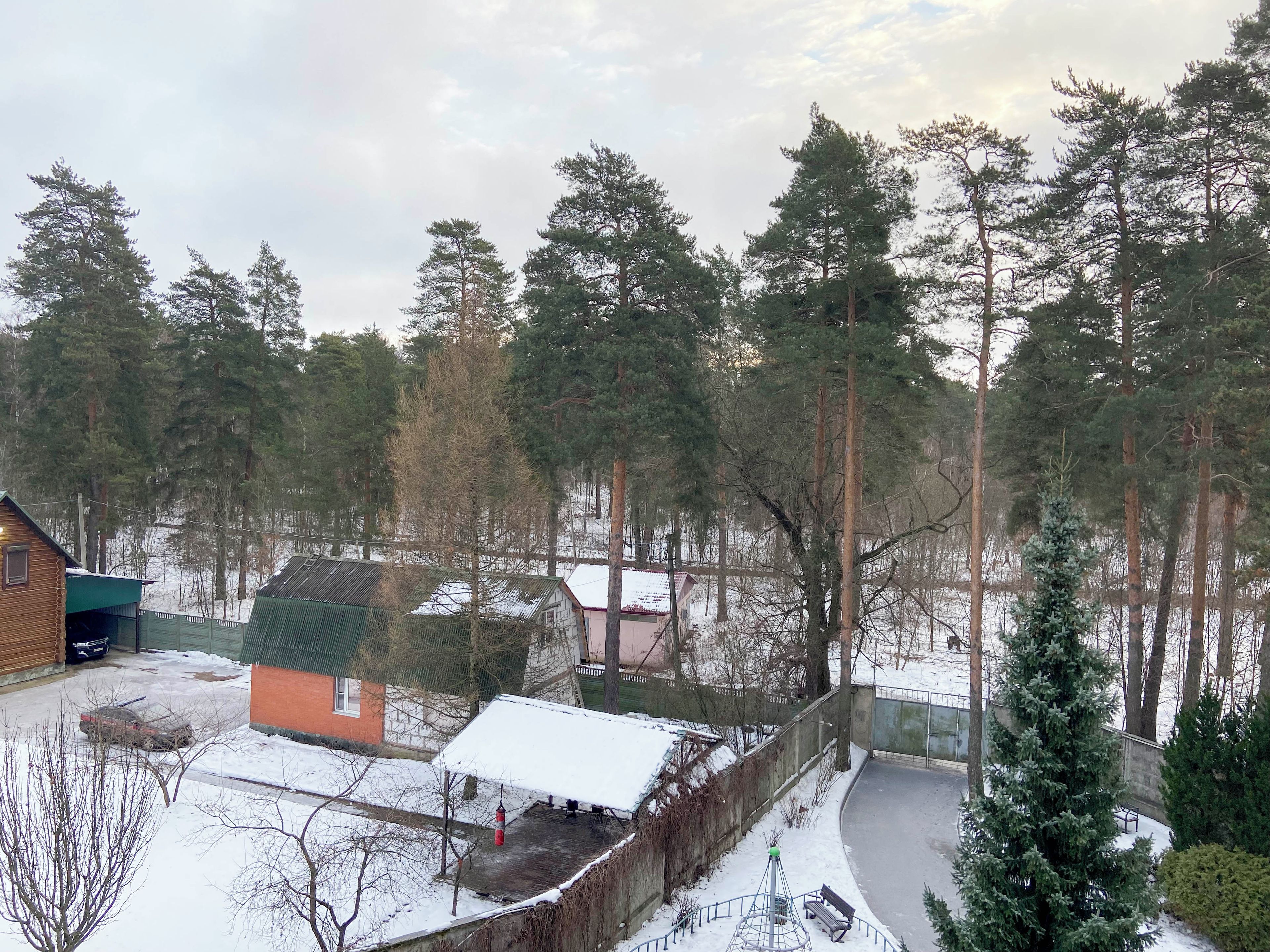 A residential area with a small house, a fenced yard, and a snow-covered ground.