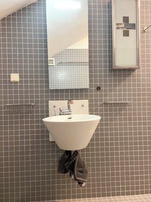 Un baño con un lavamanos blanco, un espejo y un perchero para toallas.